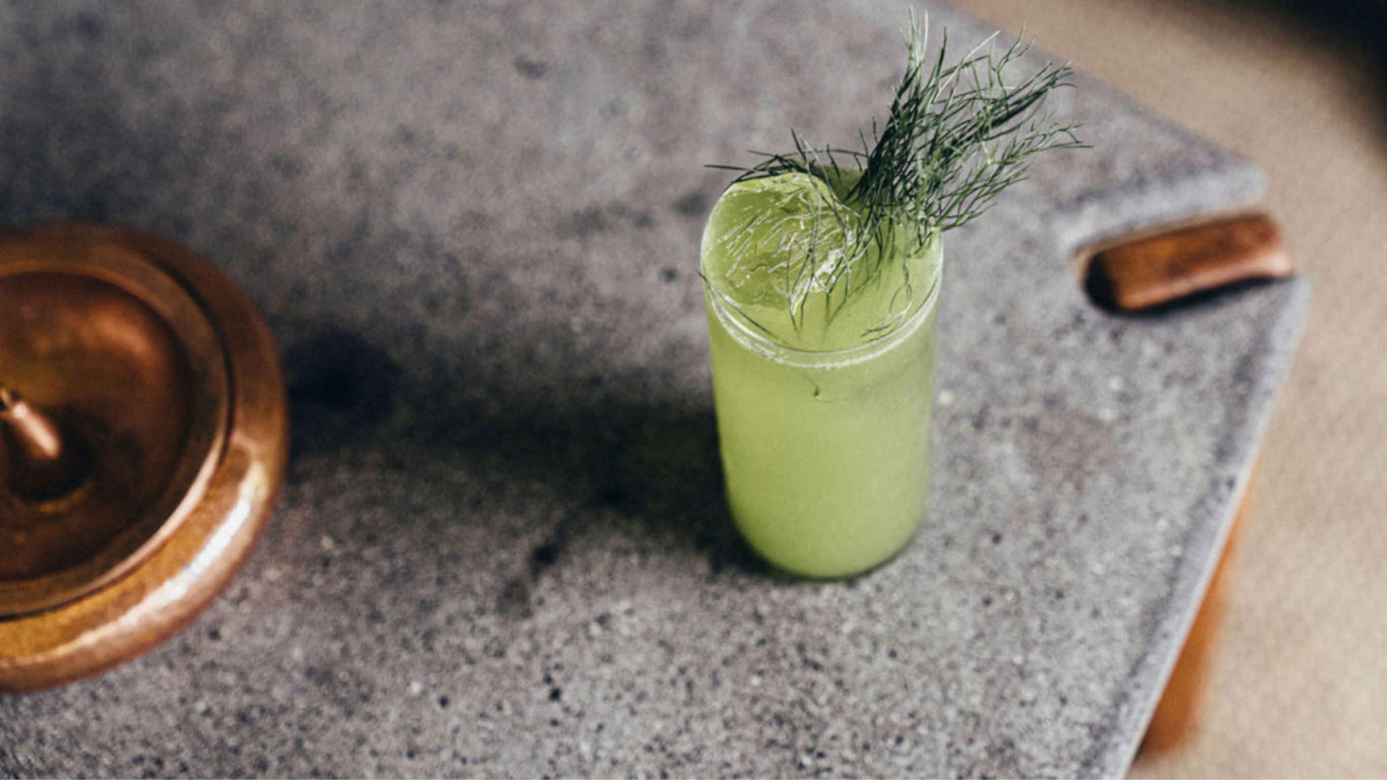 Cóctel verde con guarnición de hierbas sobre mesa lateral de piedra 